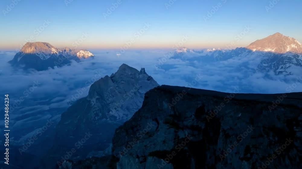 Poster The first rays of sun are illuminating the snow capped peaks of a mountain range, while the valley below is still covered by a thick sea of clouds