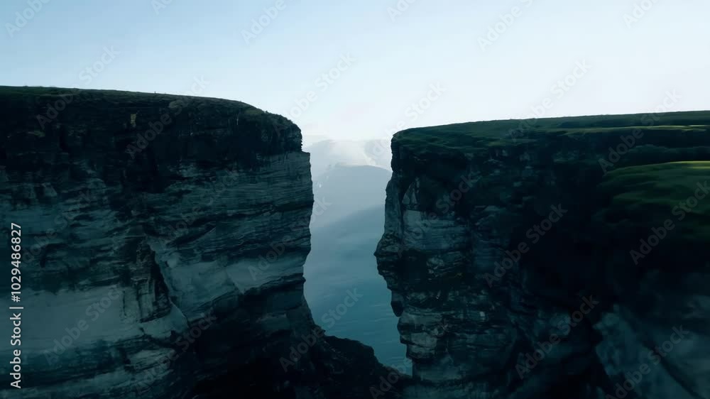 Poster sunlight illuminating a narrow canyon separating two steep cliffs, one with lush green grass and the