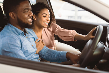 Fototapeta premium Buying Car. Joyful African American Spouses Testing New Vehicle Sitting In Auto In Store. Selective Focus