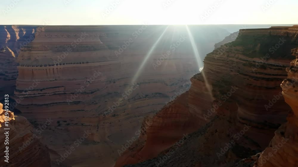 Poster The sun's rays burst over a stunning canyon. Casting a warm glow on rocky formations with a beautiful lens flare. Illuminating the dramatic erosion of sandstone cliffs in shades of orange. Red