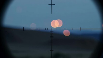 Sniper scope is aiming at a city in the distance, with the lights blurred by the optics and a body of water in the foreground