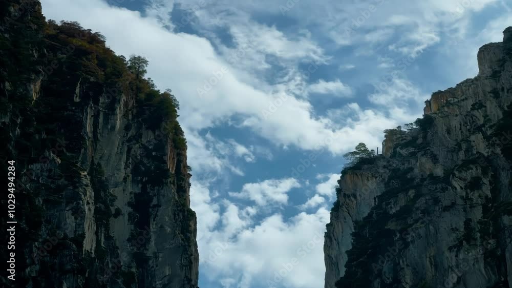 Poster two massive cliffs stand tall and proud under a blue sky with fluffy white clouds. evoking awe and w