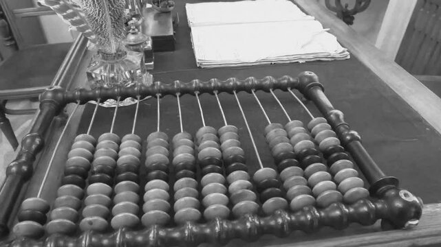 Old abacus, counting frame lies on the table in office. Black and white video in retro style with cinema effects, old filming. Close-up view highlights an antique wooden abacus with well-worn beads