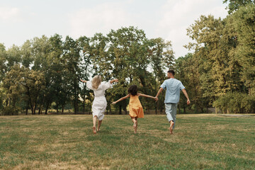 A joyful family runs hand in hand through a lush green park.