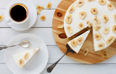 Delicious banana cake with coffee cup on table top view. Sliced fruit biscuit with caramel and buttercream on wooden catering plate, copy space