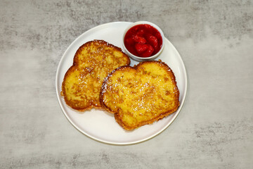 Two pieces of French toast and strawberry syrup on the side served on a white plate.