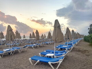 Blue lounge chairs and folded umbrellas on the hotel's empty beach in the evening. Beach vacation...