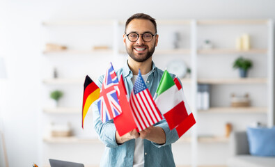 Modern education and student exchange. Cheerful young Caucasian guy holding bunch of different...