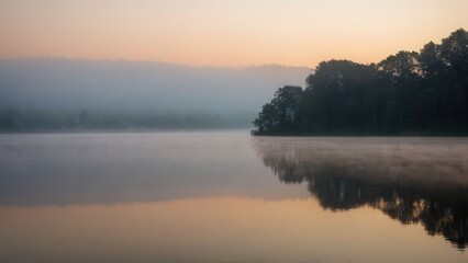 Fototapeta premium Soft morning fog hovering over a tranquil lake, reflecting the silhouette of distant trees. This peaceful scene blends the stillness of water with the mystique of fog in a natural, quiet setting