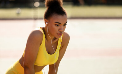 Active Training. Tired African American young woman in yellow sportswear bra and headphones resting...