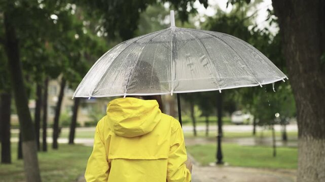 girl under umbrella. Slow motion. rain city park. view from back. young woman hiding under umbrella from raindrops. walk slush. rainfall rain. bad cloudy weather. man walks through wet streets park
