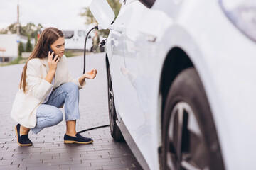 Woman Charging Electric Car While Talking on Smartphone