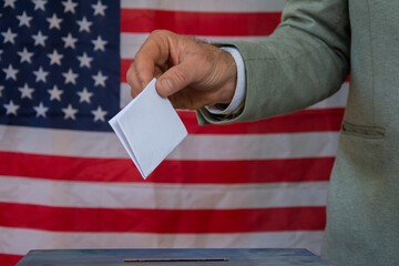Hand placing vote in ballot box with USA flag in background  election concept