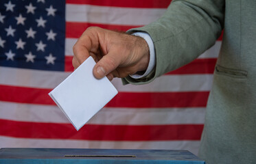 Hand placing vote in ballot box with USA flag in background  election concept