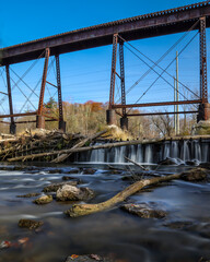 Railroad bridge over a dam waterfall. A long exposure autumn scenery.