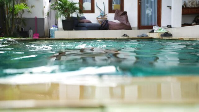 Woman enjoy swim in the pool on backyard her Villa. Relax time during sunny day. Girl emerges from water. Woman rises from the pool, eyes closed, with water streaming off their face.
