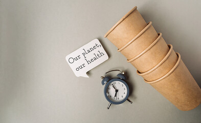 A clock sits on a table next to a stack of paper cups