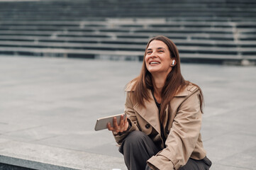 Fototapeta premium Happy businesswoman listening music on earphones outdoors using smartphone