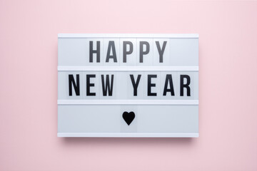 Lightbox with the text HAPPY NEW YEAR on pastel pink background. Minimal Christmas or New Year concept.