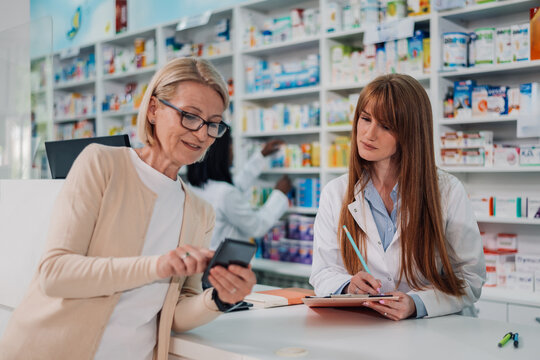 Senior woman showing her phone screen to pharmacist in drugstore - Powered by Adobe
