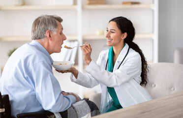 Medical assistance for elderly people with disabilities. Young nurse feeding senior handicapped man...