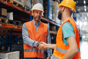 Two warehouse workers shaking hands in distribution center