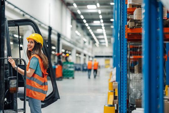 Female warehouse worker climbing onto forklift in busy warehouse - Powered by Adobe