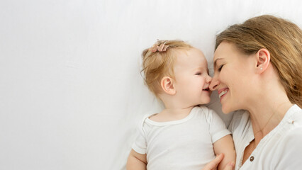 Happy motherhood. Loving young mother lying with her pretty little baby girl on the bed, enjoying maternity leave, top view, panorama with free space