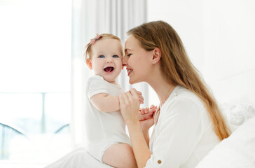 Beautiful mother with her baby girl hugging and bonding on the bed at home. Mother's care and love,...