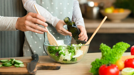 Daddy and little daughter cooking veggie salad together in kitchen, adding olive oil, cropped image, closeup