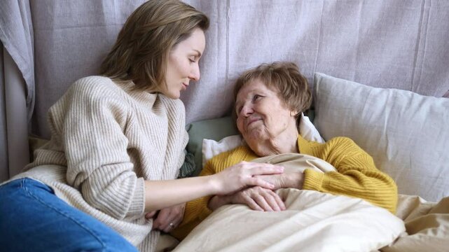 Daughter cares for bedridden mother, shows support with words and presence nearby. Attention to mother during difficult times. Family support, care for elderly mother, overcoming difficulties together