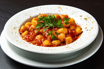 Gnocchi dish with tomato sauce and parsley on rustic wooden table.