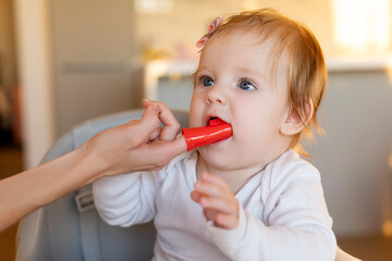 Mother brushing baby girl teeth with finger brush, mom doing oral hygiene to smiling little kid at...