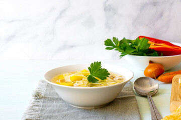 Chicken soup with noodles and vegetables in white bowl
