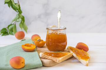 Homemade apricot jam in glass jar on kitchen white background. Summer harvest and canned food. 