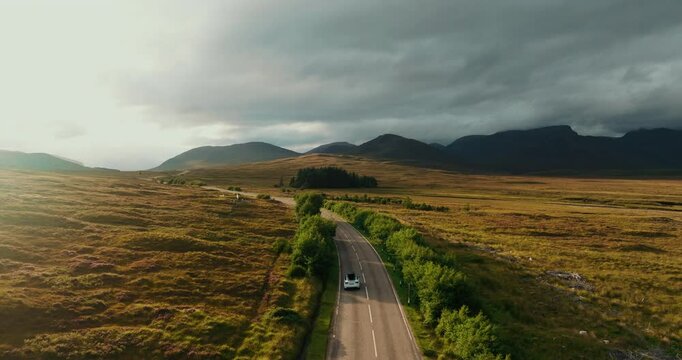 Breathtaking view from above of white car moving on NC500 in sunny Scottish landscape on moody day