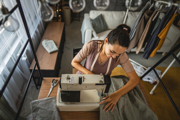 Obraz premium Adult woman tailor sewing clothes on electric sewing machine