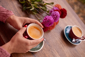 A woman's hands are holding a cup of tea. In the background there are flowers