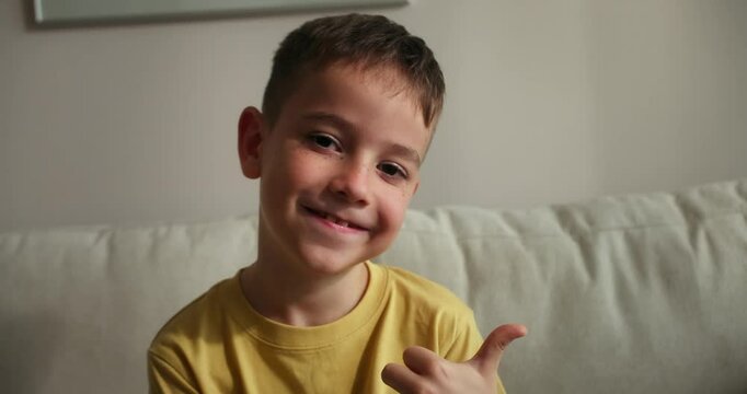 Portrait of a very happy little boy, smiling child looking at the camera, sitting on the sofa at home, cute child with a beautiful face sitting on the sofa. Happy childhood concept. 4K