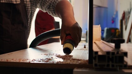 African american woodworker cleaning spindle moulder machine after finishing client commissioned project. Manufacturer using vacuum cleaner on wood shaper, sucking sawdust, camera B close up