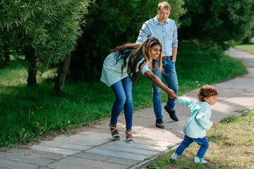 Multi-ethnic, African-American and European family walking down the road holding hands. Black baby, mother, father together in the park.