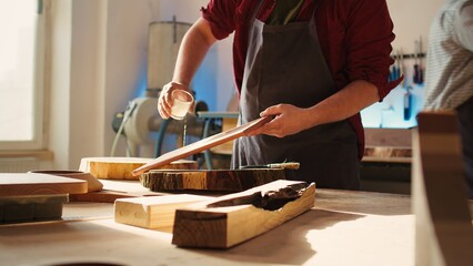 Woodworking specialist applying varnish on wood to build up protective layer. Cabinetmaker in assembly shop lacquering wooden board after sanding surface to ensure smoothness, close up shot, camera B