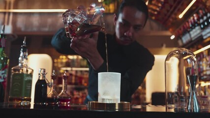 Asian bartender pouring mixed cocktail whiskey into cool glass textured cooling ice drink making special advertisement creative focusing alcohol refresh showcase at luxurious warm light pub. Vinosity.