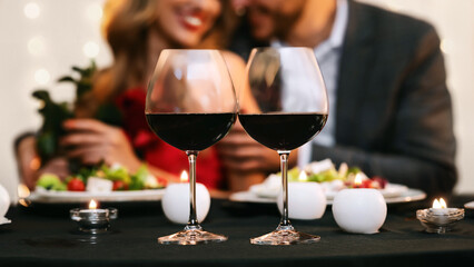 Romantic Date Background. Couple enjoying romantic dinner in restaurant, selective focus on two red wine glasses on table, panorama