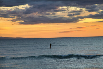 Fototapeta premium Distant paddle boarder silhouetted against a maui sunset sky.