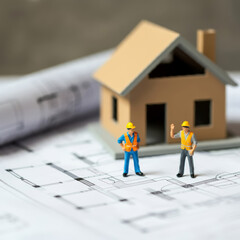 Toy workers are doing construction work on the site, house under construction on blueprints building project.