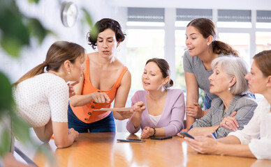 Women of different ages in casual clothes discussing documents at table in office