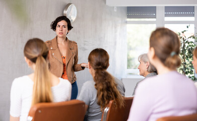 Fototapeta premium Adult woman speaker in casual clothes gives lecture in front of audience in office