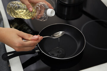 Woman with spoon pouring oil into frying pan on cooktop in kitchen, closeup