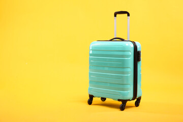 One new turquoise suitcase on yellow background, space for text